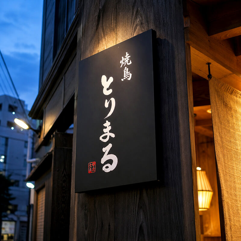焼鳥 とりまるのプレート看板。夜景の中で黒地に毛筆書きの白文字